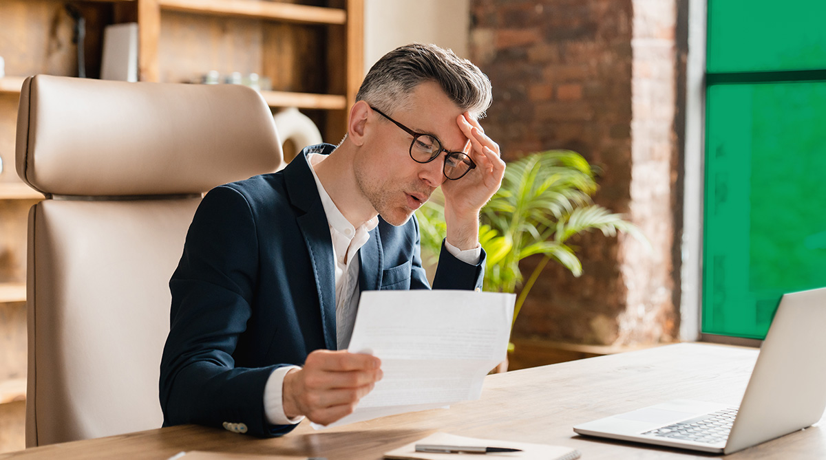 man looking at paperwork and computer and looking concerned