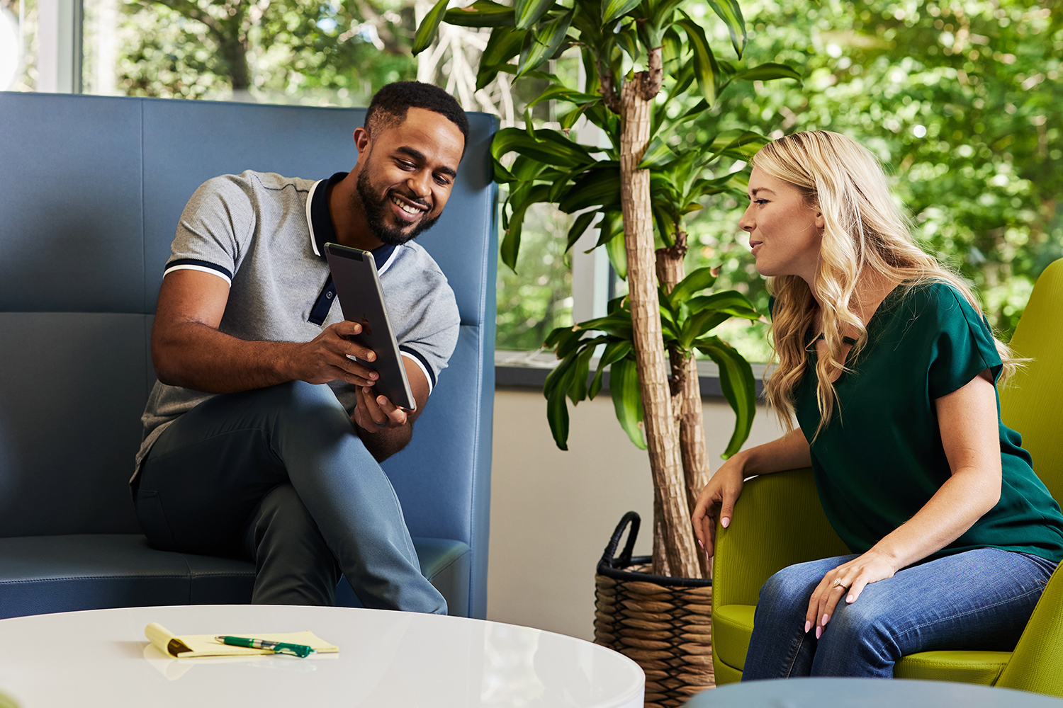 A man and woman sit in a modern office lounge, smiling at a tablet displaying the new Launch Kit. The man holds the tablet as the woman leans in to see it, surrounded by greenery and soft seating—an inviting space perfect for future buyers.