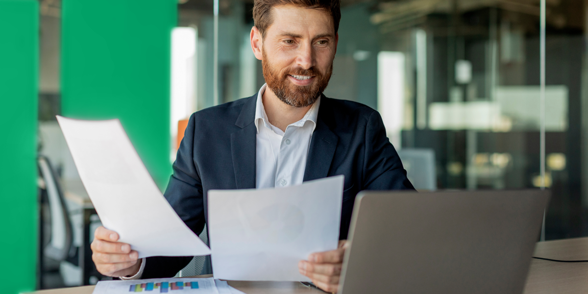 man shuffling papers while smiling at a laptop