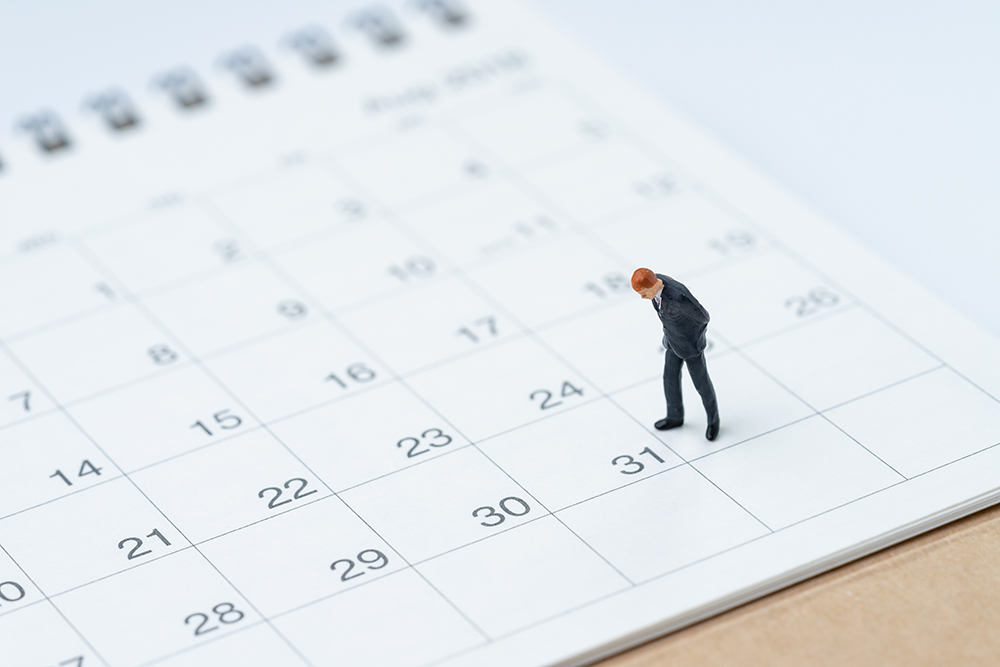 A small figurine in a suit stands on a 2026 calendar, contemplating the true cost of each date.